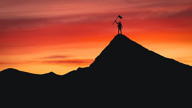 une silhouette noire brandissant un drapeau en haut d'une montagne avec un coucher de soleil